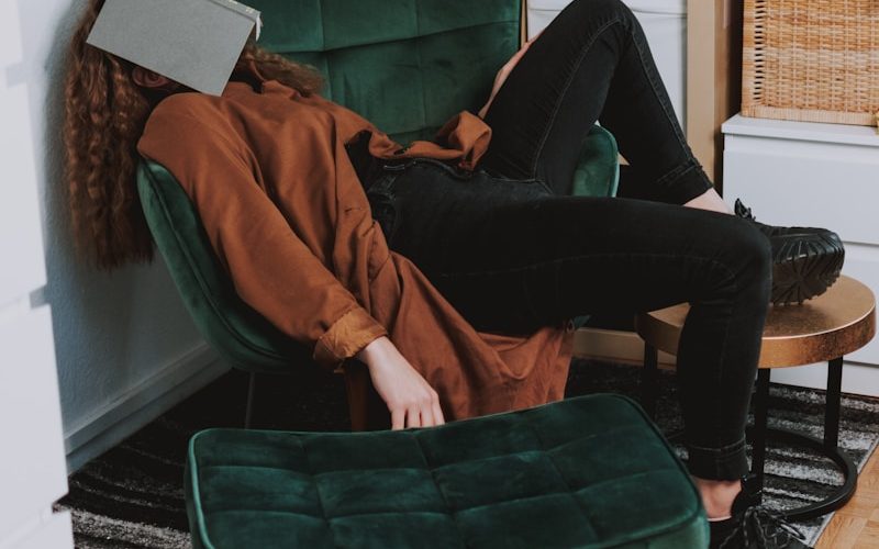 woman in red jacket and black pants sitting on green sofa chair